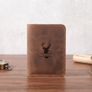 May include: A brown leather wallet featuring a laser-engraved silhouette of a deer head above the name Richard. The wallet has rounded corners and visible stitching along the edges, presenting a matte, textured surface with a natural finish.