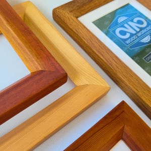 Może przedstawiać: Zbliżenie kilku drewnianych ramek do zdjęć w różnych odcieniach brązu i beżu. Jedna ramka wyświetla tekst "WOOD WORKING" i logo. Ramki są ustawione pod kątem, prezentując połączenia narożne i usłojenie drewna.