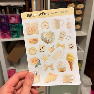 May include: A sticker sheet with various butter yellow themed illustrations, including a gift box, button, mug, candy, macaron, heart, paper clip, bow, smiley face, ice cream cone, cupcake, rose, star, perfume bottle, pie slice, and teacup. The text "Butter Yellow" is at the top.