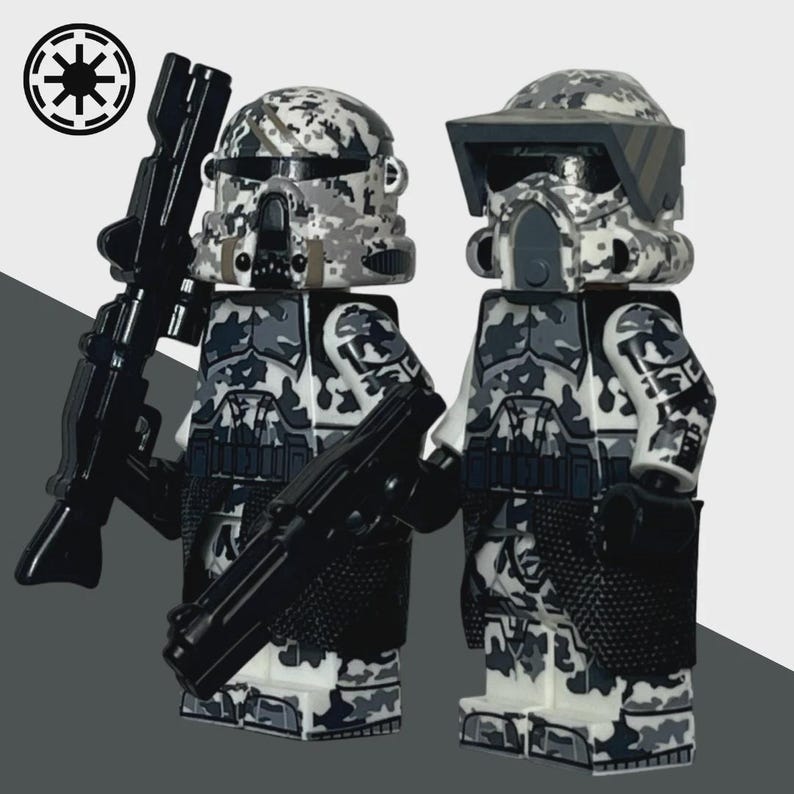 May include: Two minifigure toys of soldiers in camouflage armor, holding black rifles. The helmets and armor feature a gray, white, and black camouflage pattern. The Imperial symbol is in the upper left corner.