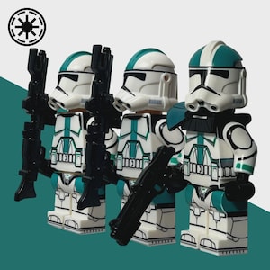 May include: Three white and teal action figures of clone troopers, each holding a black blaster rifle. The figures have white helmets with teal accents and are wearing white armor with teal detailing. A black and white symbol is in the upper left corner.