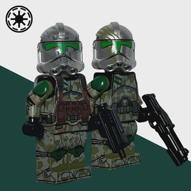 May include: Two toy soldiers in camouflage armor with silver helmets and green visors. They are holding black weapons. The soldiers are standing in front of a white and green background. A black and white symbol is in the upper left corner.