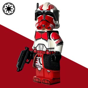 Könnte beinhalten: Rote, weiße und schwarze Actionfigur eines Soldaten mit Helm und Blasterpistole. Die Figur hat ein detailliertes Design mit roten Akzenten auf der Rüstung und dem Helm. Der Artikel ist ein Sammlerstück.