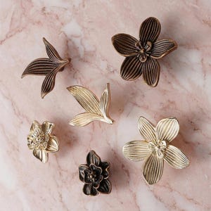 May include: A white ceramic mug with a black handle and the text "But First, Coffee" in a black, handwritten-style font. The mug is on a white surface.