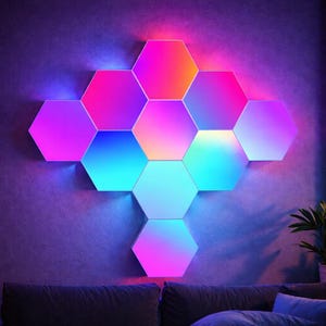 Puede incluir: Conjunto de paneles de luz LED hexagonales montados en la pared. Los paneles muestran un gradiente de colores vibrantes, incluyendo rosa, azul y morado. Las luces están sobre un sofá gris oscuro, creando una exhibición moderna y colorida.