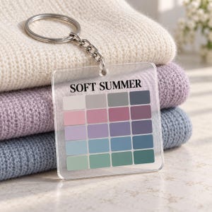 May include: A clear square acrylic keychain featuring the text SOFT SUMMER in black capital letters above a grid of twenty color swatches. The color palette includes various shades of white, gray, pink, purple, blue, and green arranged in rows.