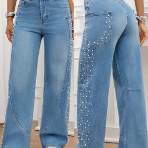 May include: Light blue denim jeans with a wide leg design. The jeans feature white pearl embellishments along the side seams and back pockets. The jeans have a classic five-pocket design and a button and zipper closure.