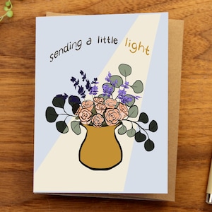 May include: Greeting card with a floral illustration. The card features a vase with pink roses, purple flowers, and green leaves. The text "sending a little light" is written on the card.