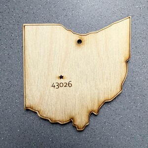 Puede incluir: Recorte de madera con la forma del estado de Ohio, con una estrella y el número 43026 grabados. Tiene un agujero para colgar. La madera es de color marrón claro natural, con bordes quemados.