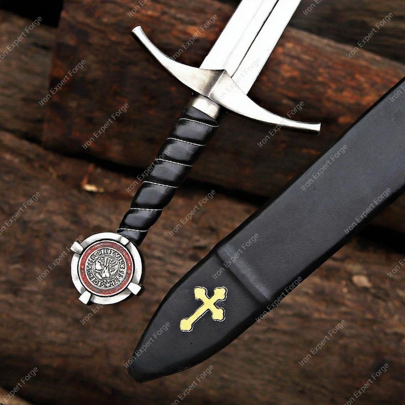 May include: A medieval-style sword with a silver blade and a black leather-wrapped handle. The hilt features a circular emblem with red and silver accents. A black sheath with a gold cross is also visible.