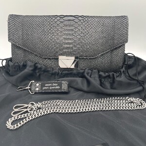 May include: A black clutch with a textured, glittery finish, a silver chain strap, and a matching keychain. The keychain reads "never lose your sparkle". The clutch has a silver clasp closure.