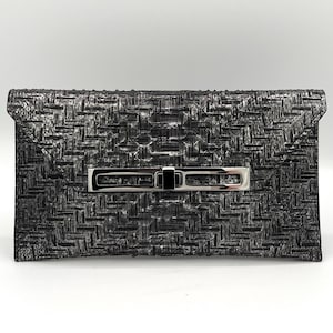 May include: A rectangular clutch with a woven texture in shades of black and silver. The clutch features a silver-toned clasp with a black center. The bag is designed with a flap closure.