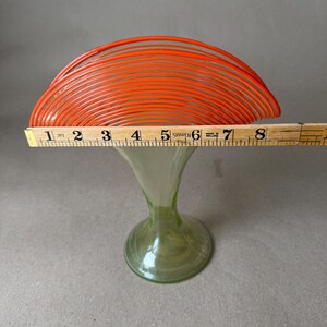 May include: A vintage art glass vase with a flared, orange top and a green, trumpet-shaped base. The orange top measures approximately 8 inches across. The vase is displayed on a neutral background.
