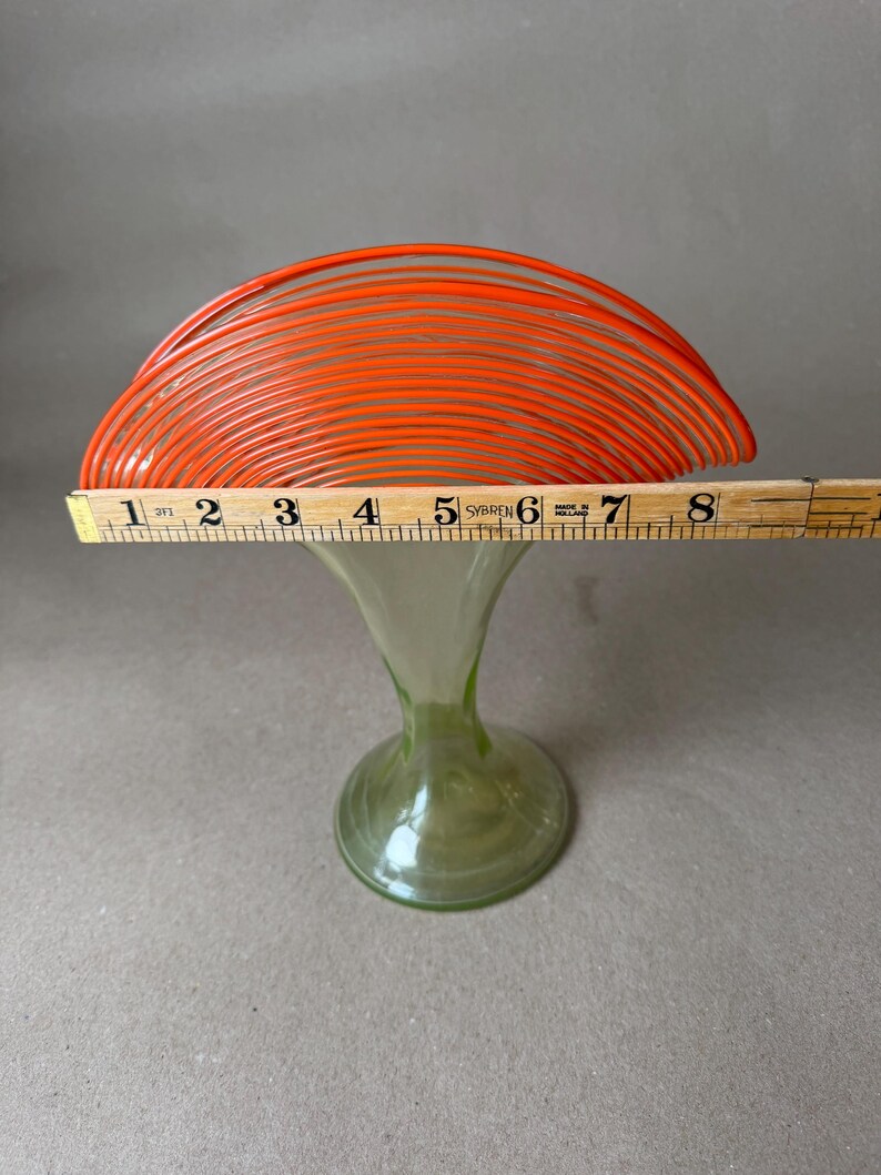 May include: A vintage art glass vase with a flared, orange top and a green, trumpet-shaped base. The orange top measures approximately 8 inches across. The vase is displayed on a neutral background.