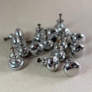 May include: A collection of small, round, polished chrome cabinet knobs. Each knob features a smooth, reflective spherical head attached to a short, threaded metal screw post, designed for mounting onto furniture or cabinetry doors and drawers.