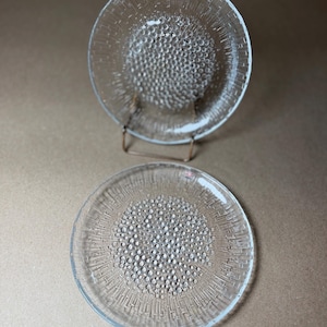 May include: Two clear glass plates with a textured, bubble-like pattern in the center and radial lines extending to the edge. One plate is displayed on a metal stand. The plates have a diameter of approximately 8 inches.