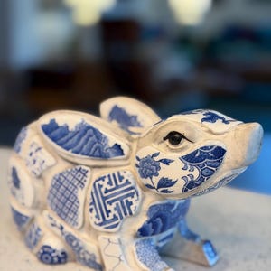 May include: A ceramic rabbit figurine in white and blue. The rabbit is decorated with various blue patterns, including floral and geometric designs. The figurine has a detailed, textured appearance and is sitting on its haunches.