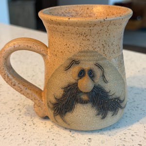 May include: A white ceramic mug with a black handle and the text "But First, Coffee" in a handwritten style. The mug is likely for hot beverages and has a glossy finish.