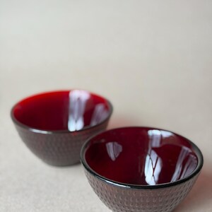 May include: Two ruby red glass bowls with a textured, dotted exterior. The bowls have a smooth, glossy interior and a dark rim. The bowls are round and appear to be empty.