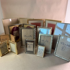May include: A collection of various rectangular metal picture frames in gold and silver tones. Several frames feature handwritten labels with dimensions in inches, such as 3 1/2 x 5, 4 1/4 x 6 3/4, 2 3/4 x 4 1/4, 3 3/4 x 5 1/2, 2 1/4 x 3 3/4, and 4 1/4 x 6 1/2.