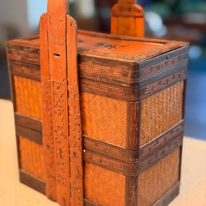 May include: A white ceramic mug with a black handle and the text "But First, Coffee" in a bold, black font. The mug is set against a blurred background, suggesting a cozy setting.