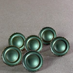 May include: A set of six round buttons featuring a smooth, matte sage green center surrounded by a metallic gold-toned rope-textured border. Each button has a raised, concave design with a distinct circular rim and a polished, reflective finish.