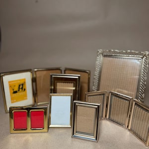 May include: A collection of gold-toned picture frames in various sizes and styles. Some frames are rectangular, others have ornate edges, and some are designed to hold multiple photos. The frames are empty, ready for display.