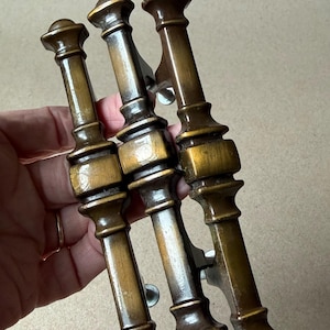 May include: Three antique bronze door pulls with a decorative, column-like design. Each pull features a rounded top and bottom, with a central rectangular section. The pulls are held together by a metal bracket.