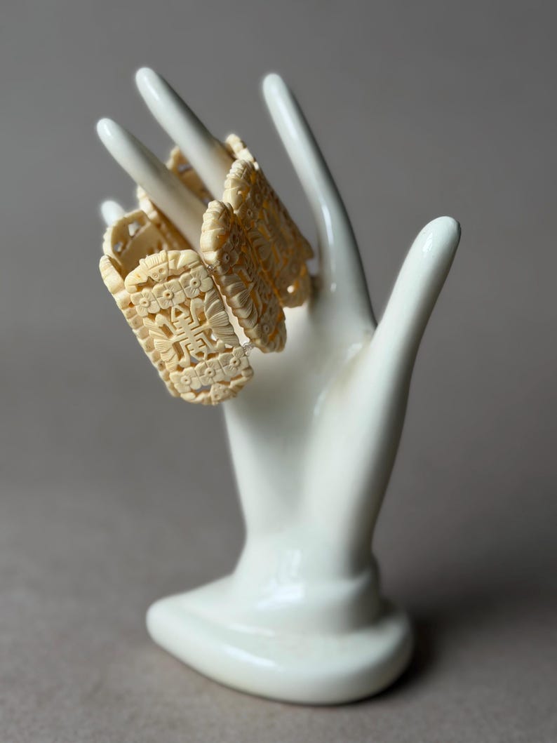 May include: A cream-colored link bracelet featuring rectangular panels with intricate carved floral patterns and central Chinese characters. The bracelet is composed of multiple connected segments, each displaying detailed relief work and a smooth finish.