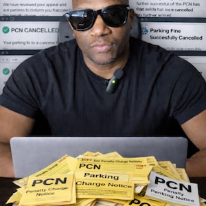 Può includere: Un uomo con occhiali da sole è seduto davanti a un laptop e a una pila di multe gialle. I biglietti riportano "PCN Penalty Charge Notice" e "Parking Charge Notice". Gli schermi dei computer dietro di lui mostrano testo sui ricorsi per le multe.