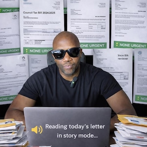 May include: A man wearing sunglasses and a black t-shirt sits in front of a laptop. The laptop screen displays the text "Reading today's letter in story mode...". Stacks of envelopes and documents surround him, with more documents in the background.