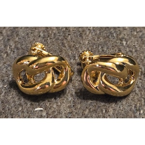 May include: A pair of gold-coloured clip-on earrings. Each earring has a linked design with a polished, reflective surface. The earrings have a classic, elegant style, suitable for various occasions.