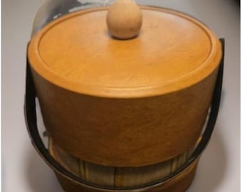 May include: A cylindrical wooden ice bucket with a smooth, light brown finish. It features a matching circular lid topped with a small, rounded wooden knob handle. A thin, dark-colored metal swing handle is attached to the sides.