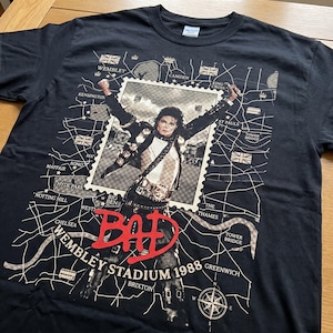 May include: Black t-shirt featuring a graphic of Michael Jackson in a stamp design. The design includes the word "BAD" in red, the text "Wembley Stadium 1988", and a map of London with landmarks.