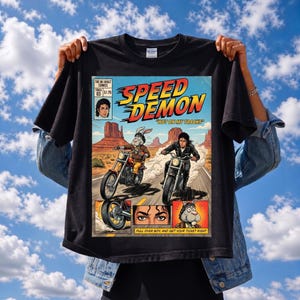 以下が含まれることがあります： 「SPEED DEMON」と「HOT ON MY TRACKS」の文字が入ったコミック風デザインの黒いTシャツ。バイク、ウサギ、人物のイラストが描かれています。シャツには「PULL OVER BOY, AND GET YOUR TICKET RIGHT」の文字も入っています。