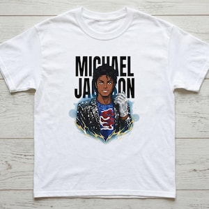 May include: White t-shirt featuring a graphic of Michael Jackson. The illustration shows Jackson in a black jacket, a silver glove, and a blue shirt with a red design. The name "MICHAEL JACKSON" is printed above the illustration in black.