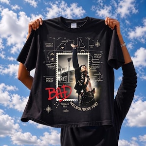 May include: Black t-shirt featuring a graphic of Michael Jackson in concert, with the word "BAD" in red. The shirt includes a map with city names and the text "MELBOURNE 1987".
