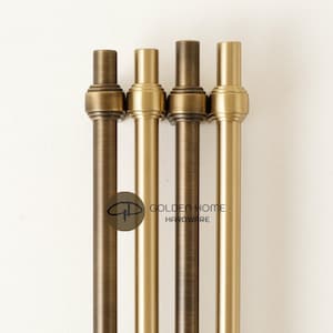 May include: Four metal rods in varying shades of bronze and gold are displayed against a white background. The rods have a cylindrical design with decorative tops. The text "GOLDEN HOME HARDWARE" is visible.