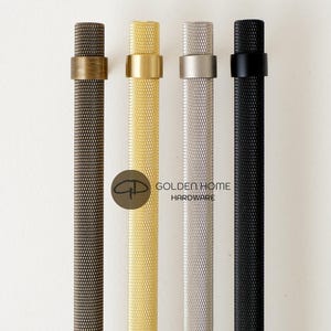 Op de afbeelding: Vier kastgrepen in brons, goud, zilver en zwart. Elke greep heeft een getextureerd, cilindrisch lichaam en een contrasterende ring aan de bovenkant. De tekst "GOLDEN HOME HARDWARE" is zichtbaar.