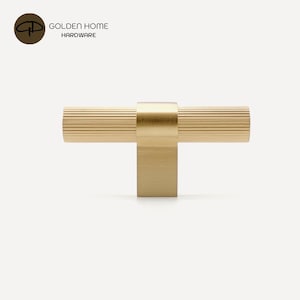 K&ouml;nnte beinhalten: Ein goldfarbener Schrankgriff mit geriffeltem, zylindrischem Griff und quadratischer Basis. Der Griff ist an einer quadratischen Basis befestigt. Das Logo "GOLDEN HOME HARDWARE" befindet sich in der oberen linken Ecke.