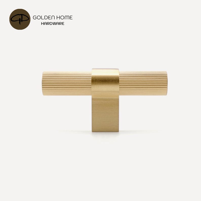 K&ouml;nnte beinhalten: Ein goldfarbener Schrankgriff mit geriffeltem, zylindrischem Griff und quadratischer Basis. Der Griff ist an einer quadratischen Basis befestigt. Das Logo "GOLDEN HOME HARDWARE" befindet sich in der oberen linken Ecke.