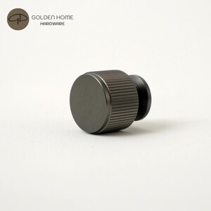 May include: A dark gray cabinet knob with a ridged cylindrical grip and a flat, circular face. The knob has a small, black, rounded base. The logo "GOLDEN HOME HARDWARE" is in the upper left corner.