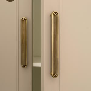 May include: Two gold-colored cabinet handles with a vertical, grooved design. The handles are mounted on a light beige cabinet door. The text "GOLDEN HOME HARDWARE" is visible in the upper left corner.