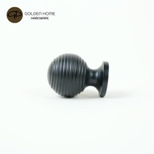 K&ouml;nnte beinhalten: Ein schwarzer, geriffelter Schrankknauf mit einer runden, kugelartigen Form und einem flachen Sockel. Der Knauf ist aus Metall und hat eine matte Oberfl&auml;che. Das Logo "GOLDEN HOME HARDWARE" befindet sich in der oberen linken Ecke.