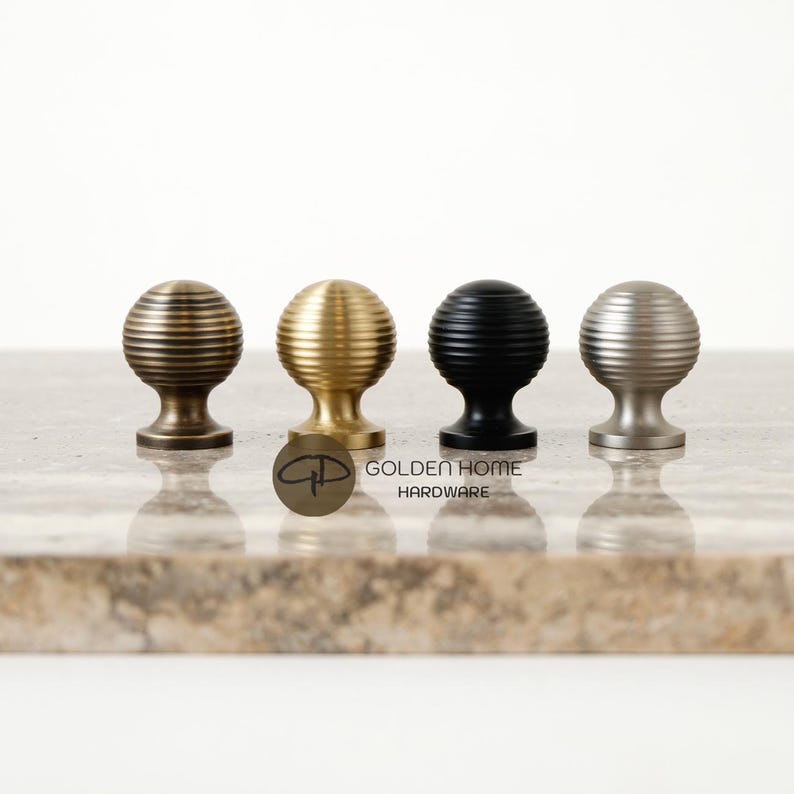 May include: Four decorative cabinet knobs in bronze, gold, black, and silver. Each knob has a ribbed, spherical design and a short, rounded base. The knobs are displayed on a light-colored surface with the "Golden Home Hardware" logo.