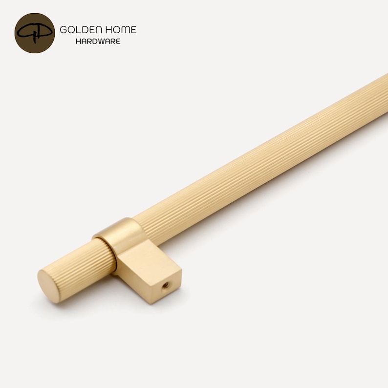 K&ouml;nnte beinhalten: Ein goldfarbener Schrankgriff mit geripptem Griff und rechteckiger Basis. Der Griff hat ein zylindrisches Ende und ist aus Metall. Der Text "GOLDEN HOME HARDWARE" befindet sich in der oberen linken Ecke.