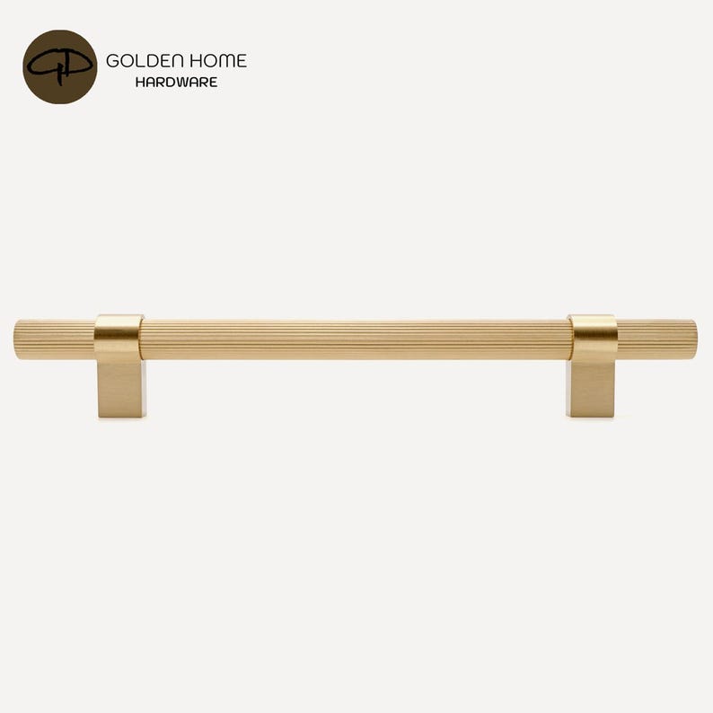 K&ouml;nnte beinhalten: Ein goldfarbener Schrankgriff mit geriffeltem, zylindrischem Griff und quadratischen Befestigungspfosten. Die Hardware hat eine geb&uuml;rstete Oberfl&auml;che und ist f&uuml;r eine einfache Installation konzipiert. Das Logo "GOLDEN HOME HARDWARE" befindet sich in der oberen linken Ecke.
