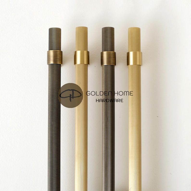 K&ouml;nnte beinhalten: Vier Schrankgriffe in verschiedenen Braun- und Goldt&ouml;nen. Jeder Griff hat einen geriffelten zylindrischen K&ouml;rper und ein goldfarbenes Band in der N&auml;he der Oberseite. Der Text "GOLDEN HOME HARDWARE" ist sichtbar.