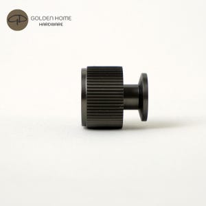 May include: A dark gray metal cabinet knob with a ridged cylindrical body and a circular base. The knob is designed for furniture hardware. The logo "GOLDEN HOME HARDWARE" is in the upper left corner.