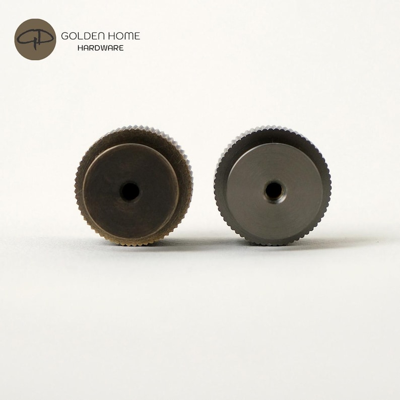 May include: Two metal cabinet knobs. One is a dark bronze color, and the other is a silver color. Both knobs have a circular design with a ridged edge and a central hole. The knobs are from Golden Home Hardware.